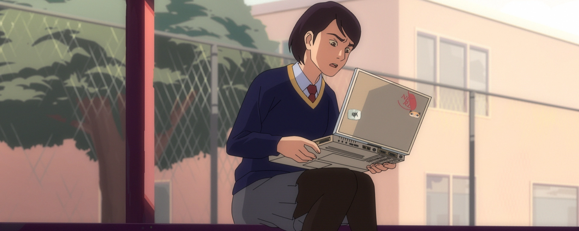 Maddie Kim sitting with her laptop. The laptop has parody stickers of the NERV logo and Maromi.